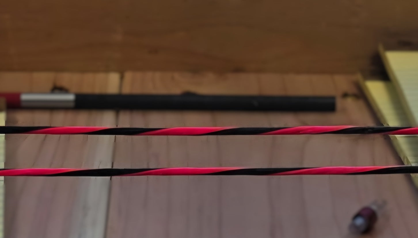 Close-up of red and black archery bowstrings against a wooden workbench