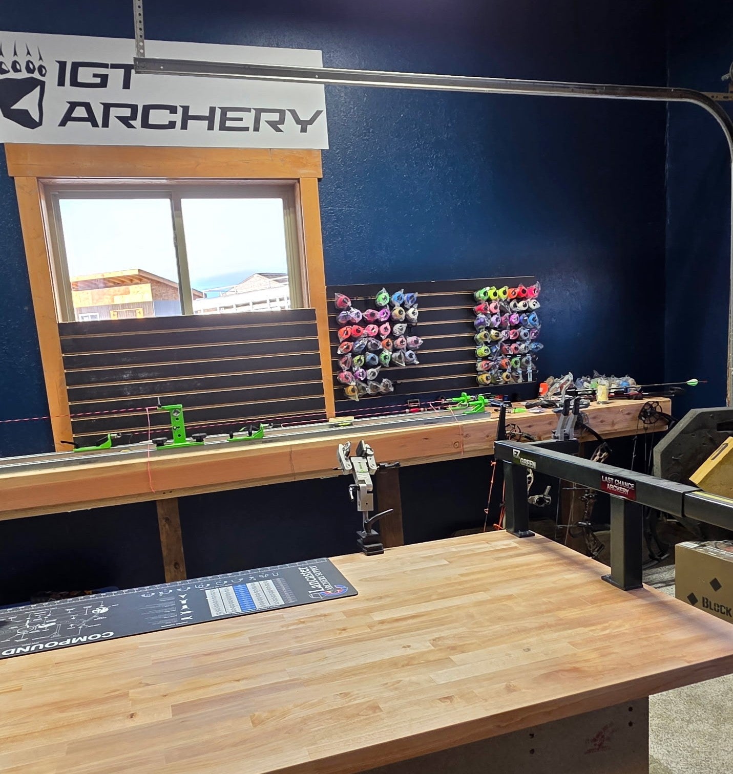 Archery range with bow stands and quiver on a wall, featuring IGT Archery branding.