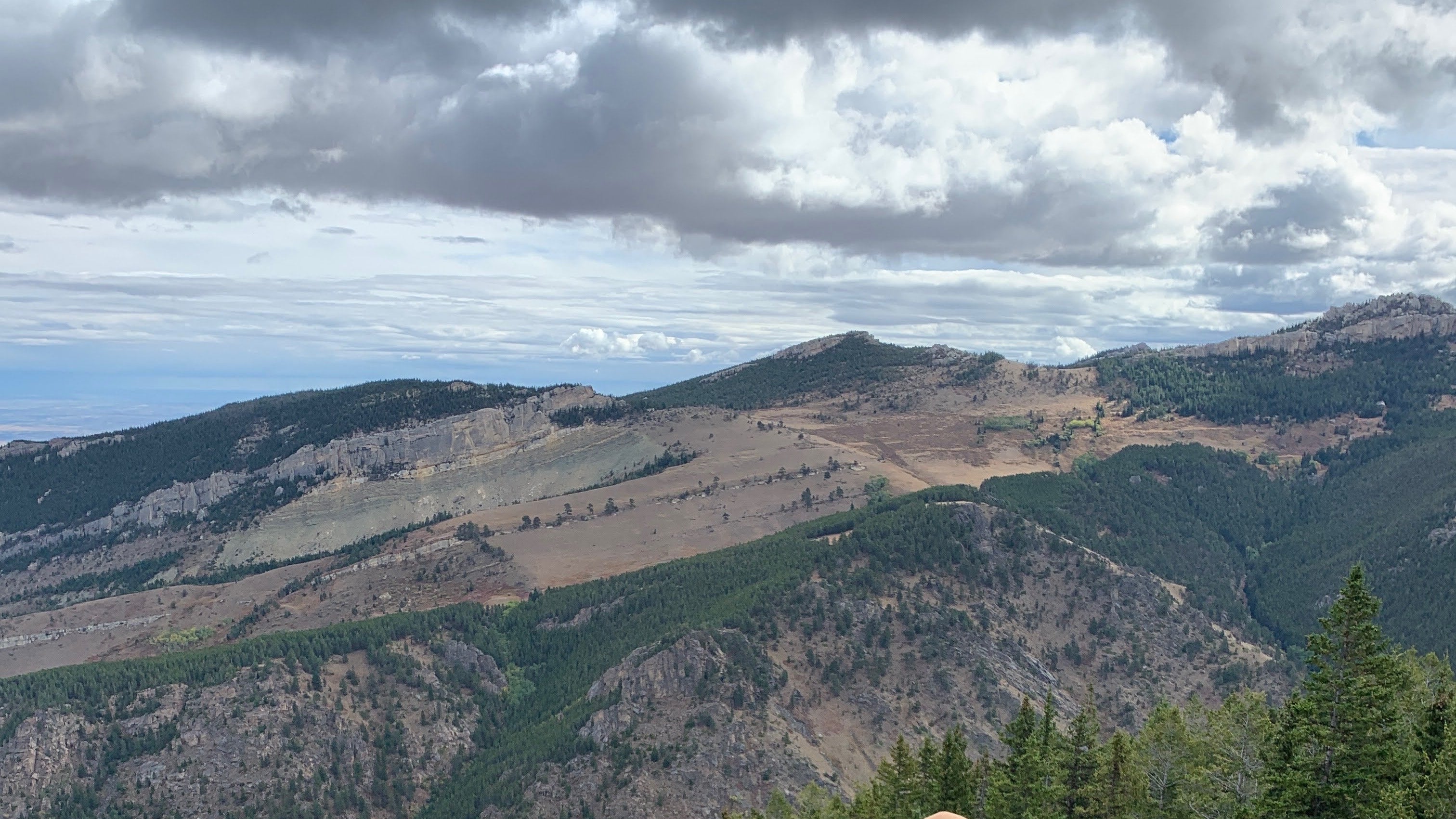 Person in camouflage gear with a bow on a rocky cliff overlooking a valley.