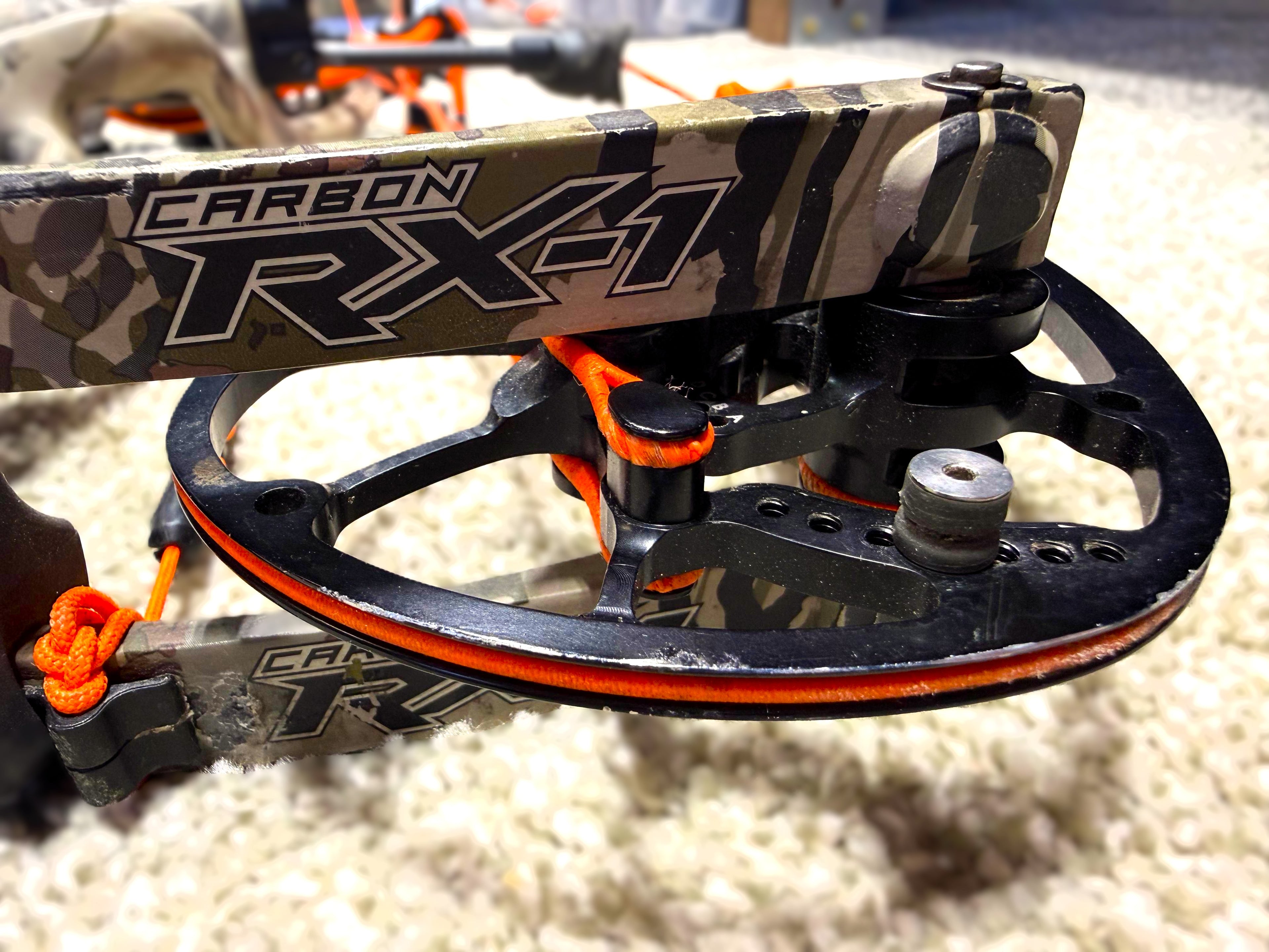 Close-up of a compound bow cam with 'Carbon RX-1' branding on a textured surface.