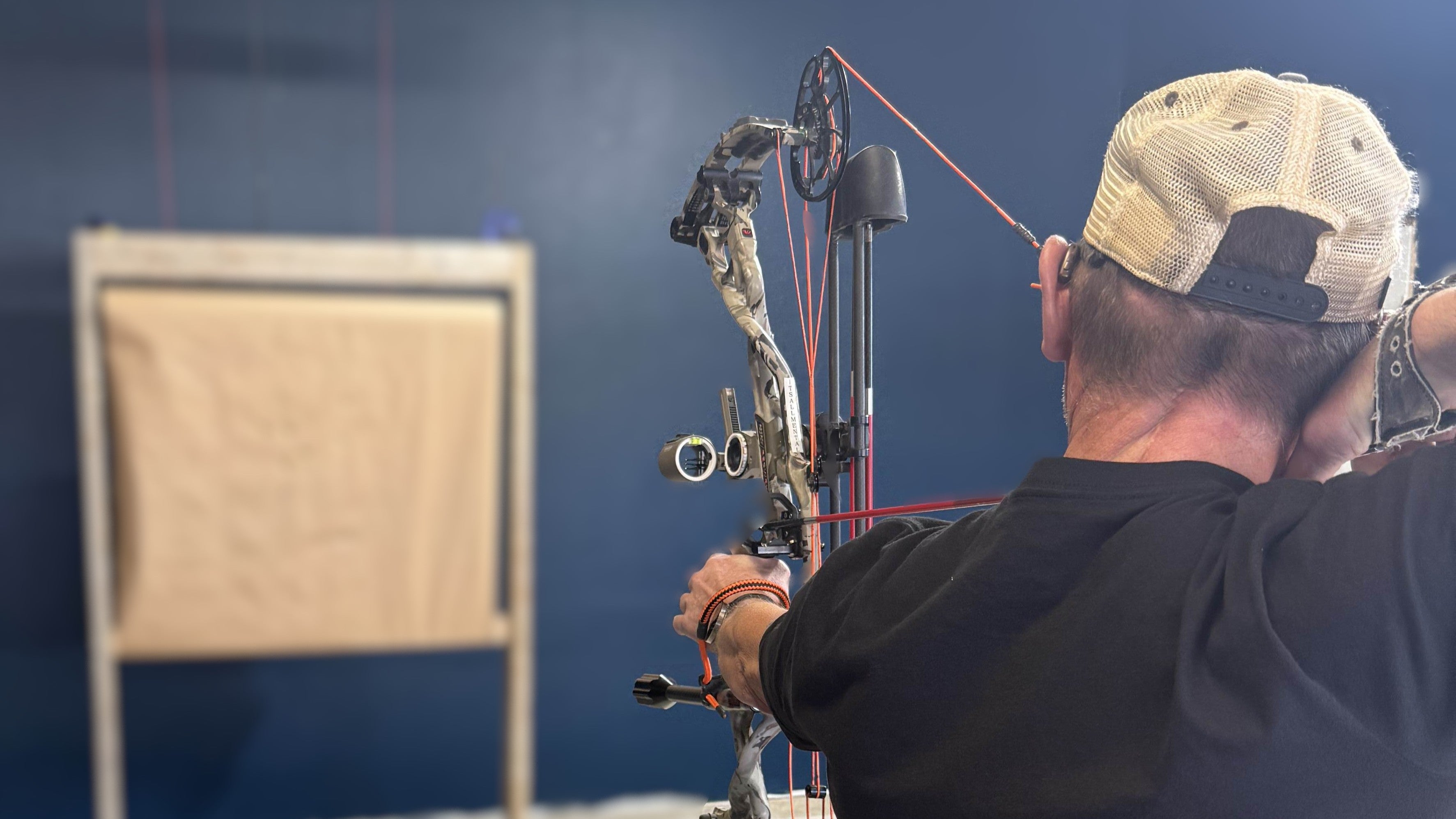 Person with a compound bow aiming at a target in an indoor setting